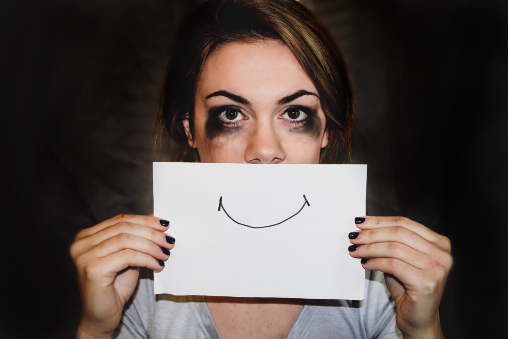 Young adult with black smudges around eyes and sheet of paper with smile over mouth