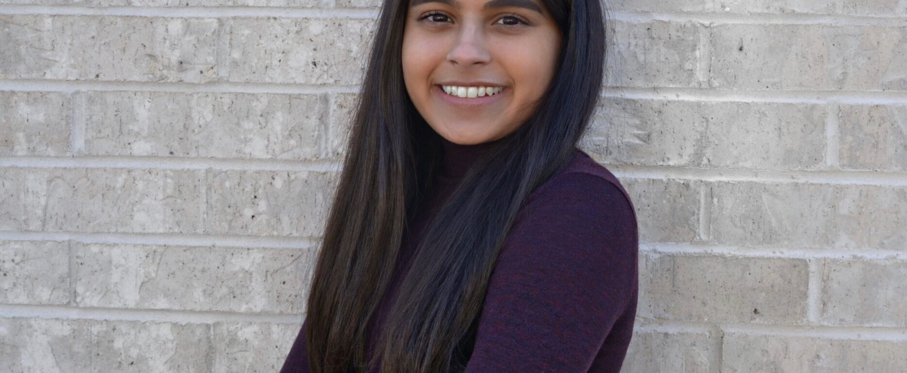 Woman with long black hair standing in front of white wall smiling