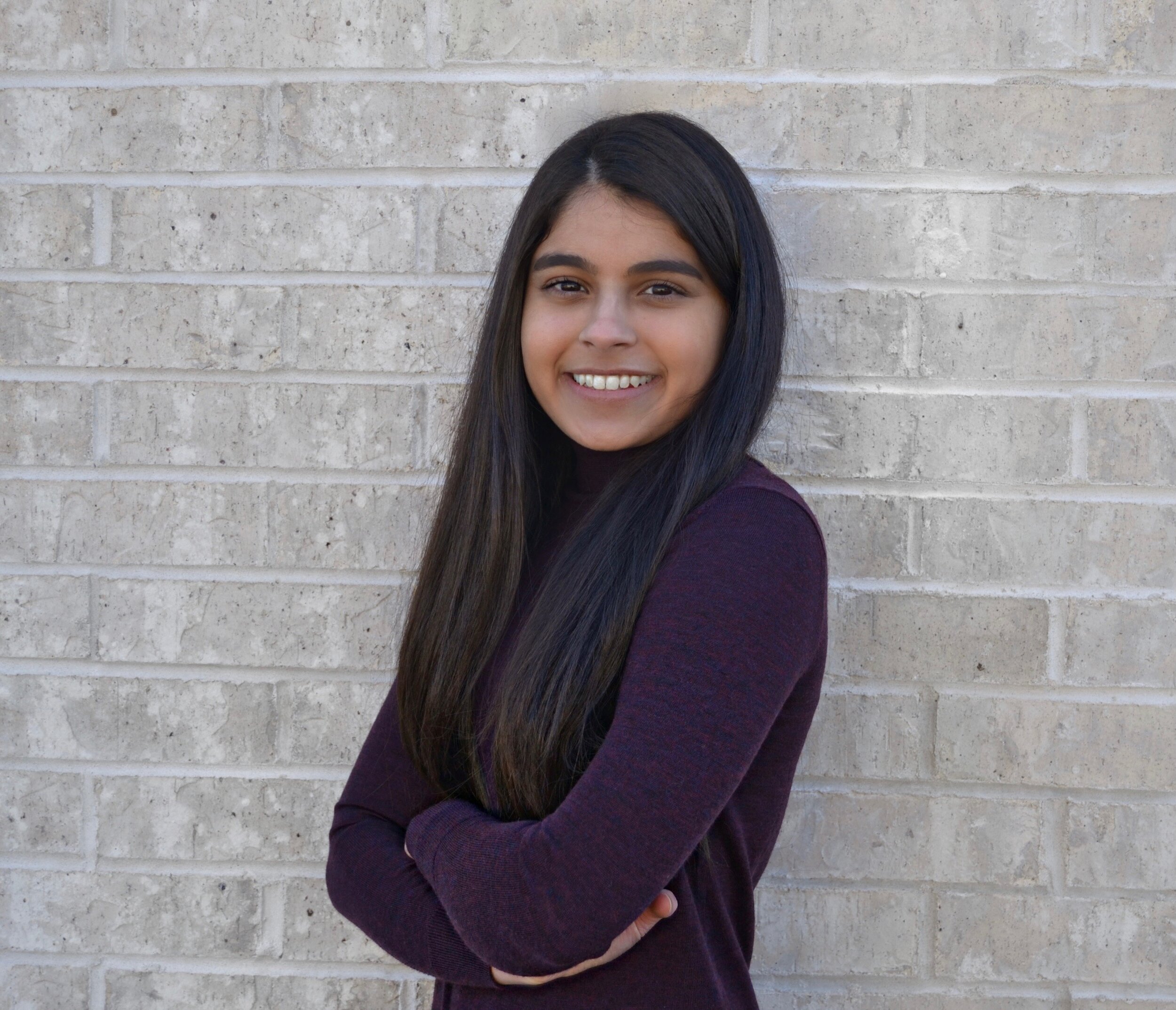 Woman with long black hair standing in front of white wall smiling