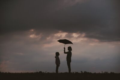 A picture containing sky, outdoor, standing, sunset. 2 people with umbrella