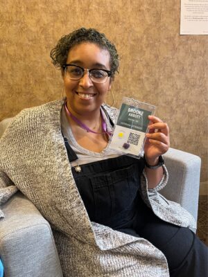 Woman, indoors, with black hair smiling and holding up name tag