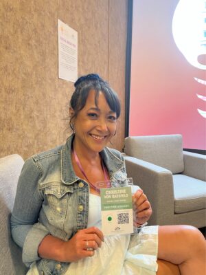 Woman, indoors, with black hair smiling and holding up name tag