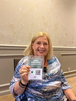 Woman, indoors, with blond hair smiling and holding up name tag