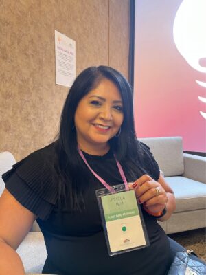 Woman, indoors, with black hair smiling and holding up name tag