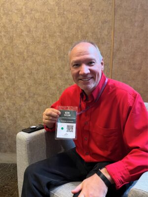 Man, indoors, balding smiling and holding up name tag