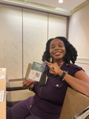 Woman, indoors, with black hair smiling and holding up name tag