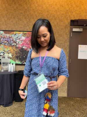 Woman, indoors, with black hair blue dress holding up name tag