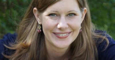 Young woman, pale, smiling, hir behind ears, dangling earrings, smiling