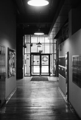 Looking down dark school hallway to bright day outside. Black and white