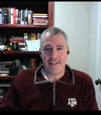 Man with short hair, ear buds, black sweater talking