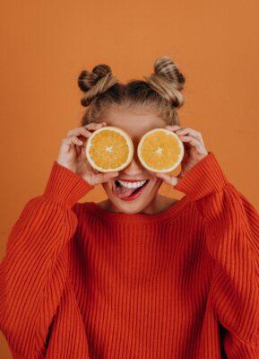 Woman in large red knitted sweater with oranges over her eyes